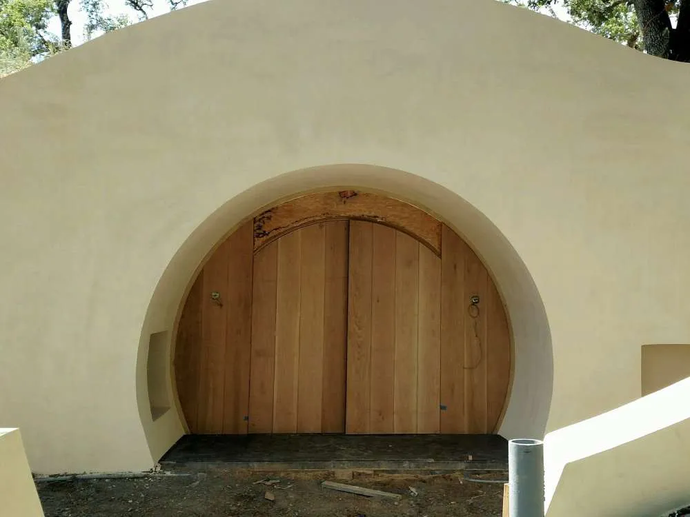 Entrance to an underground wine cave with a wooden door and smooth stucco facade in an outdoor setting.